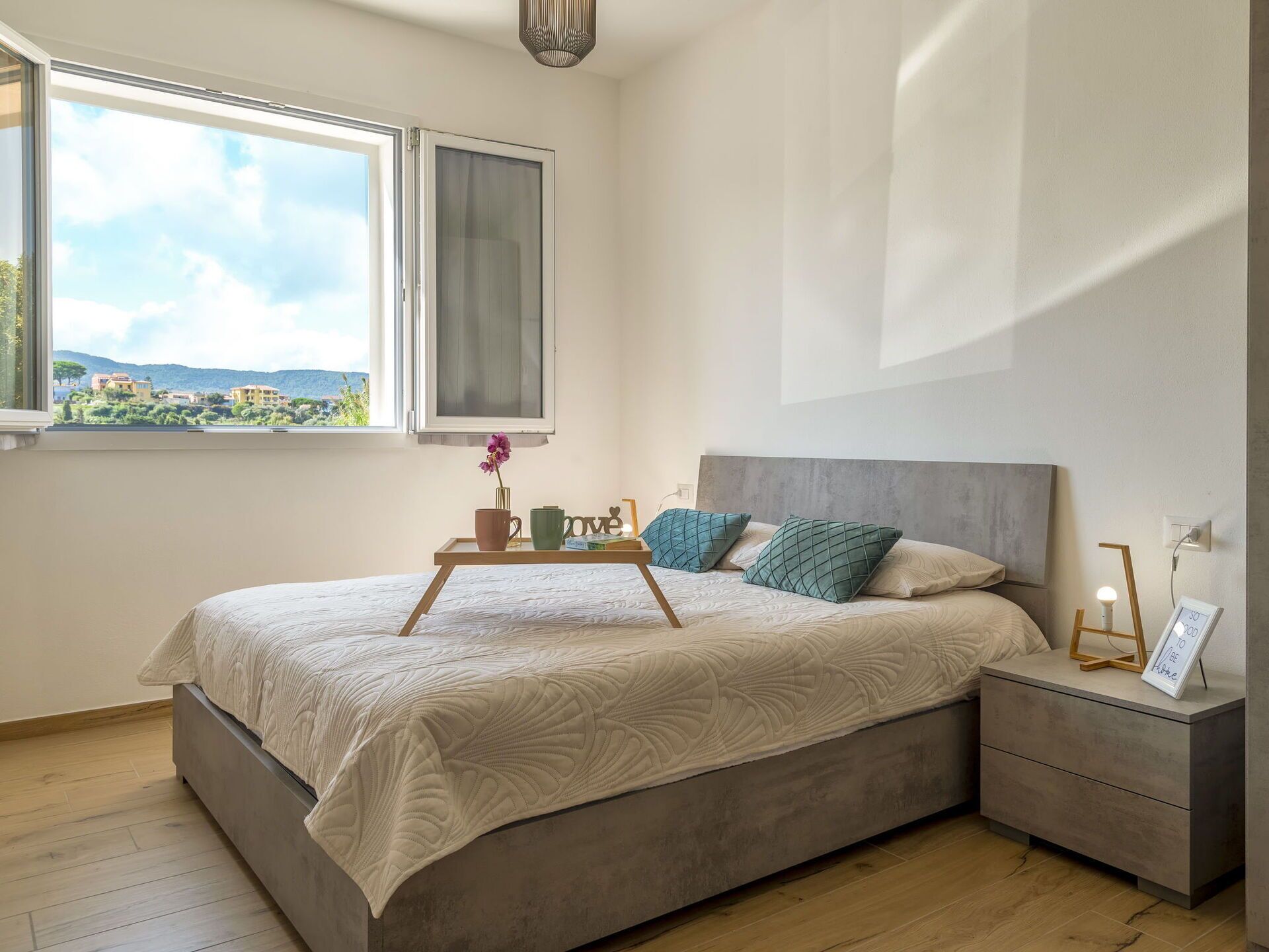 A bedroom with a bed, bedside tables, a window with a view, and a bedside lamp.