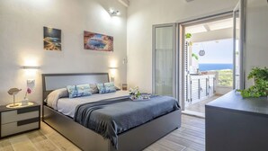 A modern bedroom with a large bed, bedside tables, and a view of the sea through an open balcony. - Nice apartment for 5 people with WIFI, A/C, TV and patio (Valledoria)