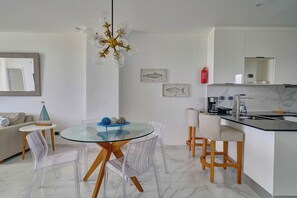 Een moderne keuken met witte kastjes, een marmeren aanrecht en een glazen eettafel met transparante stoelen.