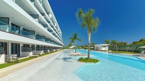 A modern hotel with a swimming pool, multiple balconies, and palm trees. - Cana Rock Star - Golf - Piscina - Playa (Punta Cana)