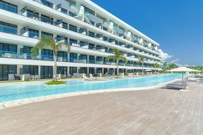 Een modern hotel met een groot zwembad, meerdere balkons en buiten zitplaatsen.