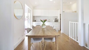 A modern kitchen with white cabinets, a wooden dining table, and a vase with flowers. - Chic Elwood Escape by Ready Set Stay (Elwood)