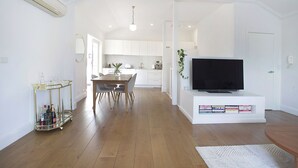 A modern living room with a flat-screen TV, a dining area with a glass-top table, and a kitchen in the background. - Chic Elwood Escape by Ready Set Stay (Elwood)