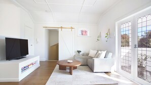 A modern living room with a flat-screen TV, a round wooden coffee table, a white sofa, and a large sliding glass door with a view of the outdoors. - Chic Elwood Escape by Ready Set Stay (Elwood)