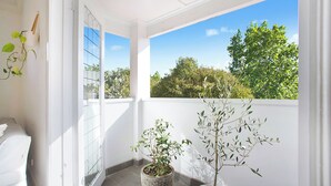 A balcony with two potted plants, a white wall, and a clear view of trees and sky. - Chic Elwood Escape by Ready Set Stay (Elwood)