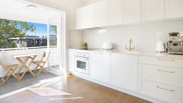 A modern kitchen with white cabinetry, a built-in oven, a coffee machine, and a view of the city through a large window. - Chic Elwood Escape by Ready Set Stay (Elwood)
