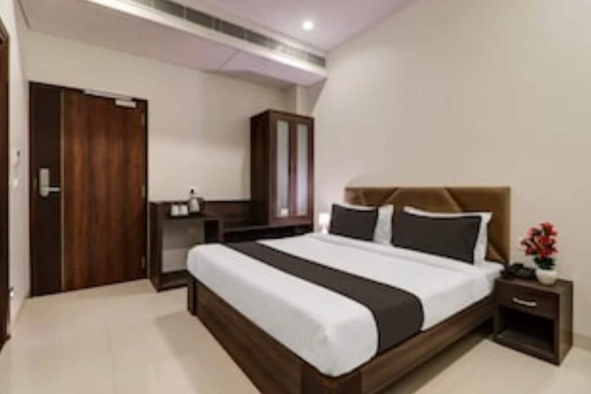 A hotel room with a large bed, a wardrobe, a bedside table with a lamp, and a small cabinet.