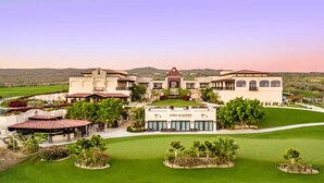 Un edificio grande con un letrero que dice "GOLF ACADEMY", rodeado de césped cuidado y senderos.