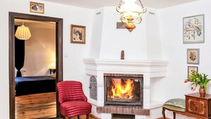 Uma sala de estar com lareira, uma poltrona vermelha, um banco de madeira e uma cama.