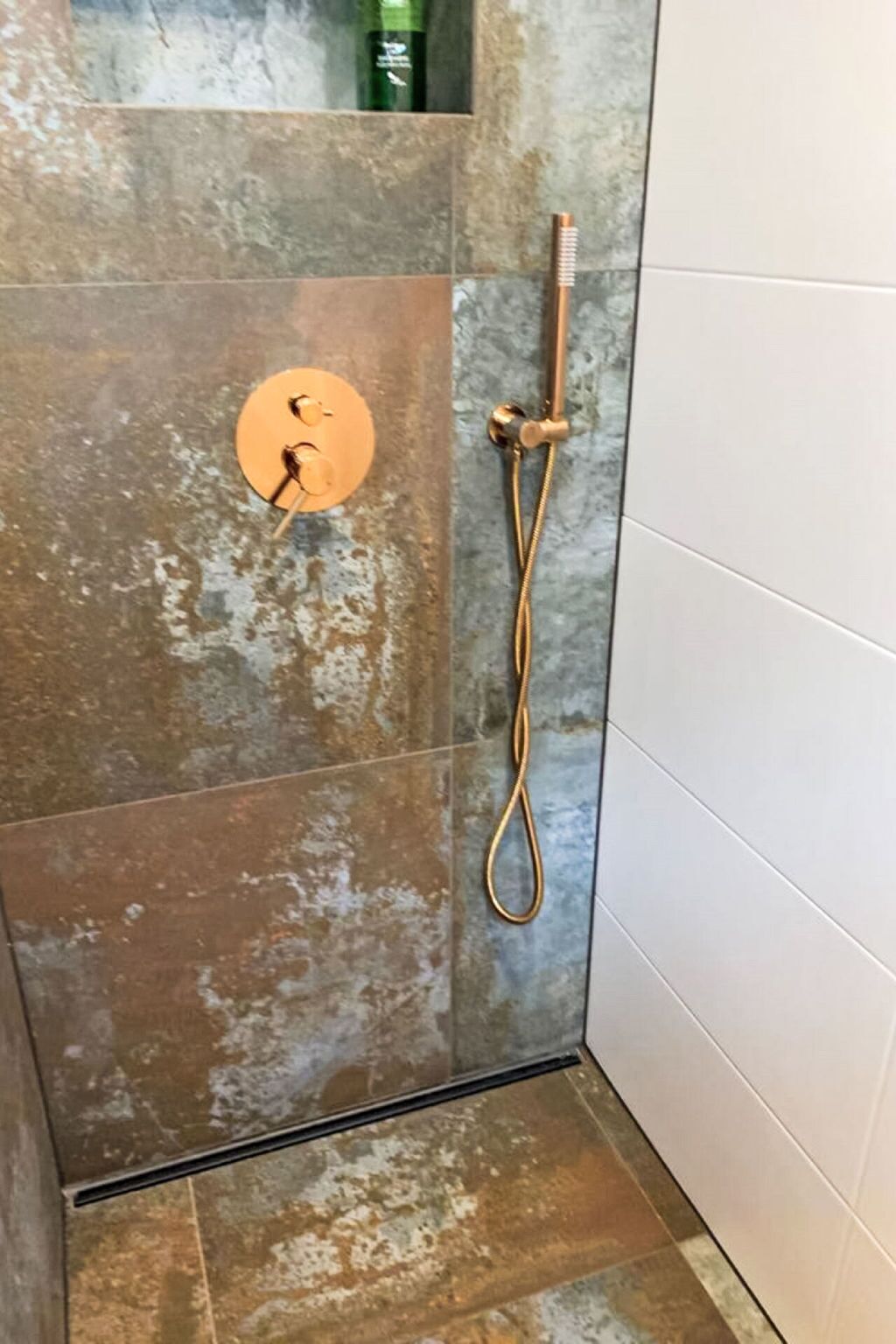 A shower with a handheld showerhead and a wall-mounted faucet.