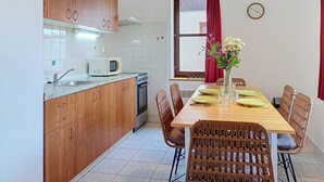 Une cuisine compacte avec des meubles en bois, un four à micro-ondes et un coin repas comprenant des chaises en osier et une table dressée pour deux personnes.