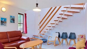 Un salon moderne avec un escalier en bois, un canapé en cuir, des chaises en bois et une petite table.