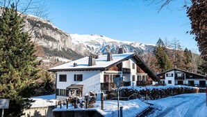 A two-story chalet with a sloped roof, a balcony, and a snow-covered driveway.