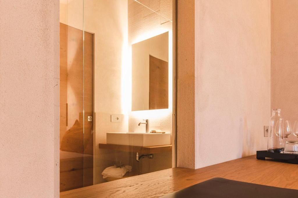 Un bagno moderno con pareti divisorie in vetro, un mobile bagno in legno, un lavandino e uno specchio.