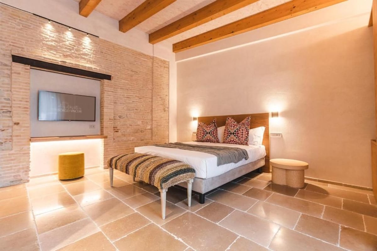 Quarto moderno com cama, mesa de cabeceira e televisão fixada na parede.