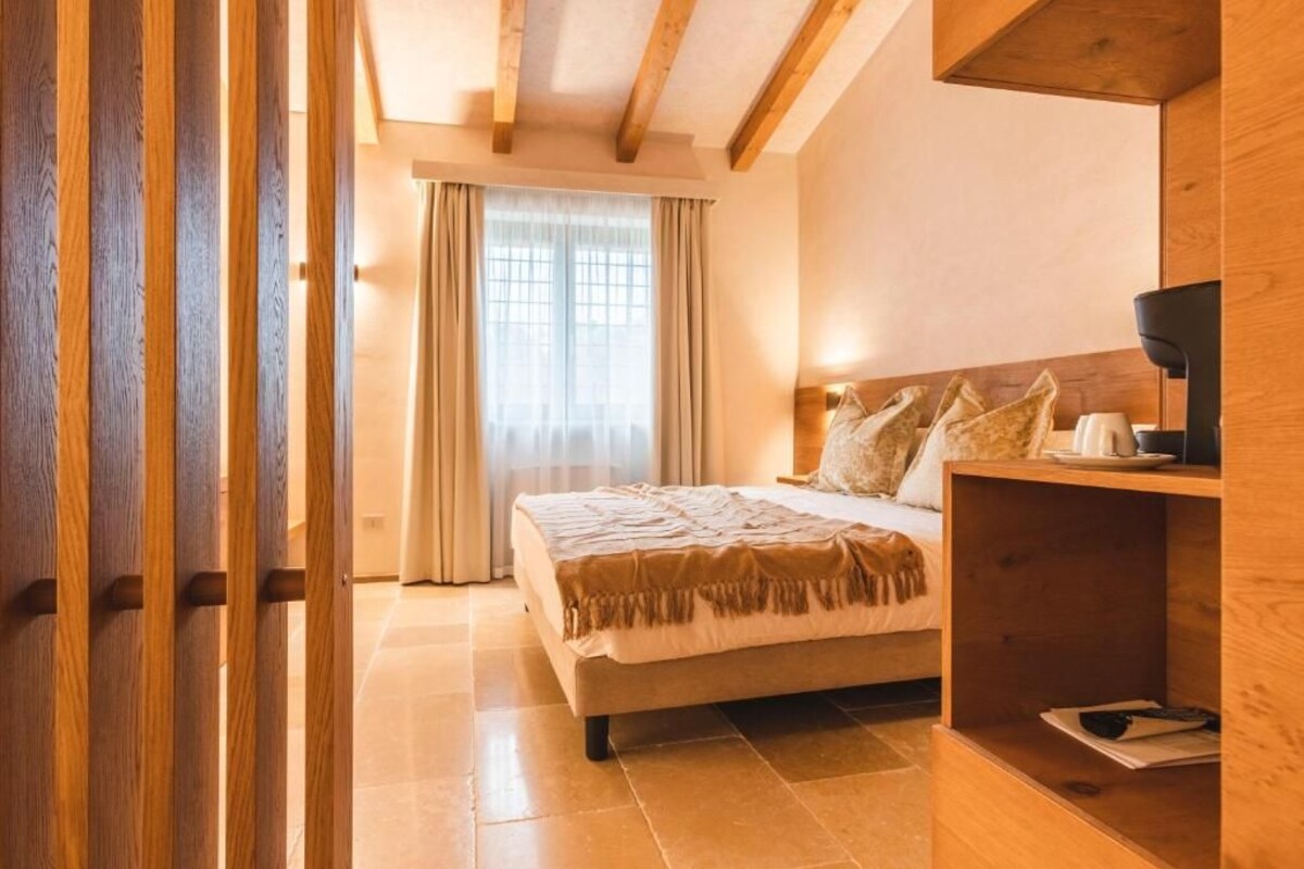 Ein Schlafzimmer mit einem Bett, einem Holzkopfteil, einem Nachttisch, einem an der Wand montierten Fernseher und einem Fenster mit Vorhängen.