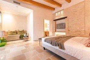 A modern bedroom with a large bed, a sofa, and a TV mounted on a brick wall. - Borgo Vinceri (Lucera)