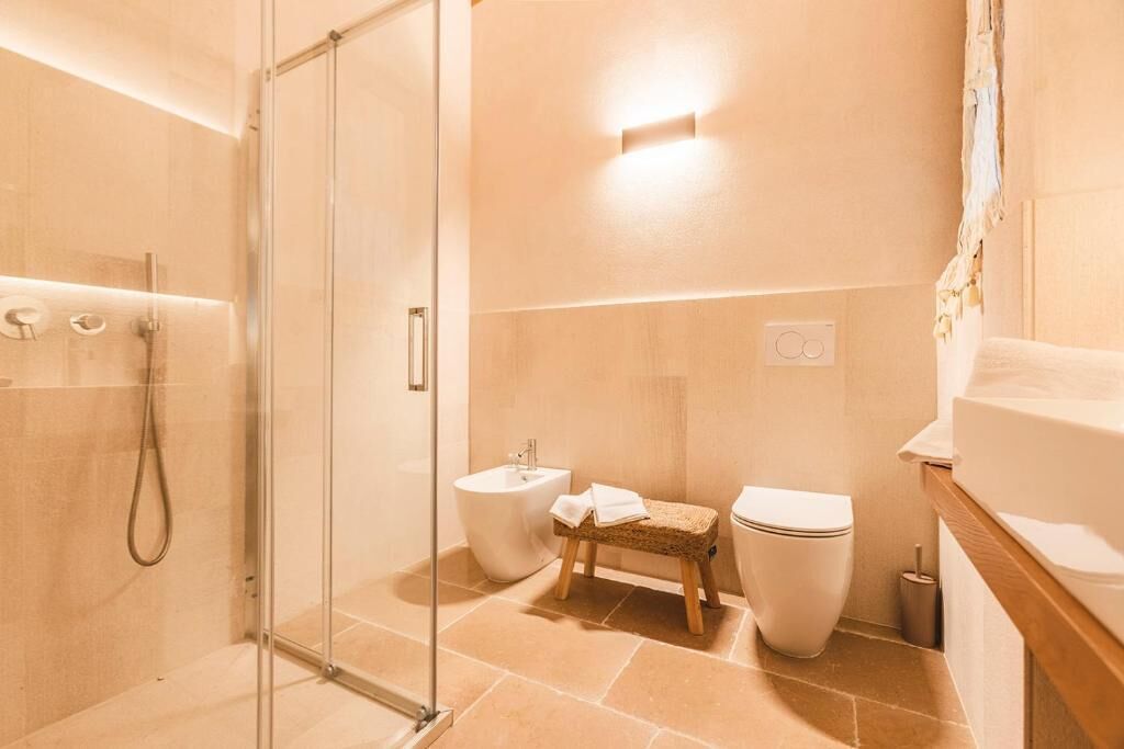 A modern bathroom with a glass shower enclosure, a bidet, a toilet, and a wooden stool.