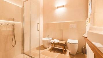 A modern bathroom with a glass shower enclosure, a bidet, a toilet, and a wooden stool.
