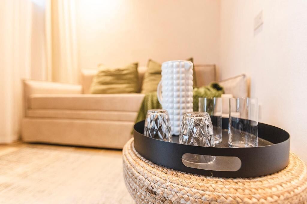 Una sala de estar con una mesa de centro tejida que sostiene saleros, pimenteros, un vaso y un candelabro. Un sofá color beige con cojines verde y blanco se ve al fondo.