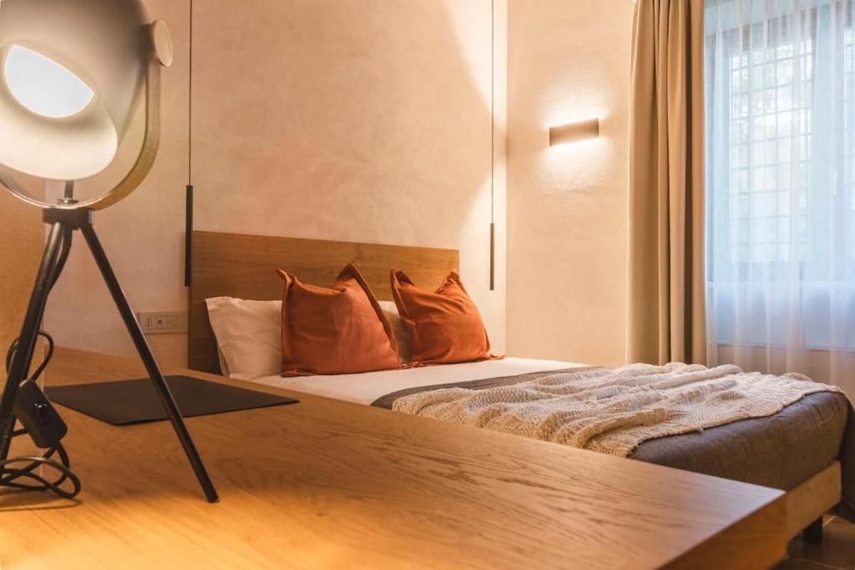 A hotel room with a wooden bed, a desk with a lamp, and a window with curtains.