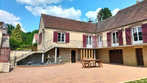 Ein zweigeschossiges Gebäude mit Innenhof, einer Treppe, die zum oberen Stock führt, und einem Essbereich mit Gartenmöbeln.