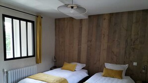 Ein modernes Schlafzimmer mit zwei Betten, einer Holzwandverkleidung, einem Deckenventilator und einem Fenster mit Vorhängen.