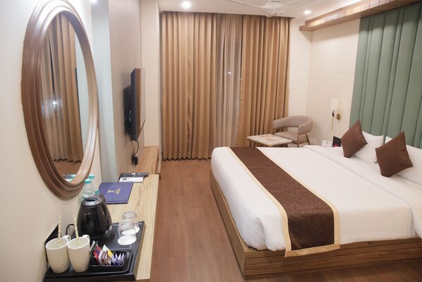 Habitación de hotel con una cama grande, un escritorio con computadora, una silla, un televisor y un ventanal con cortinas.