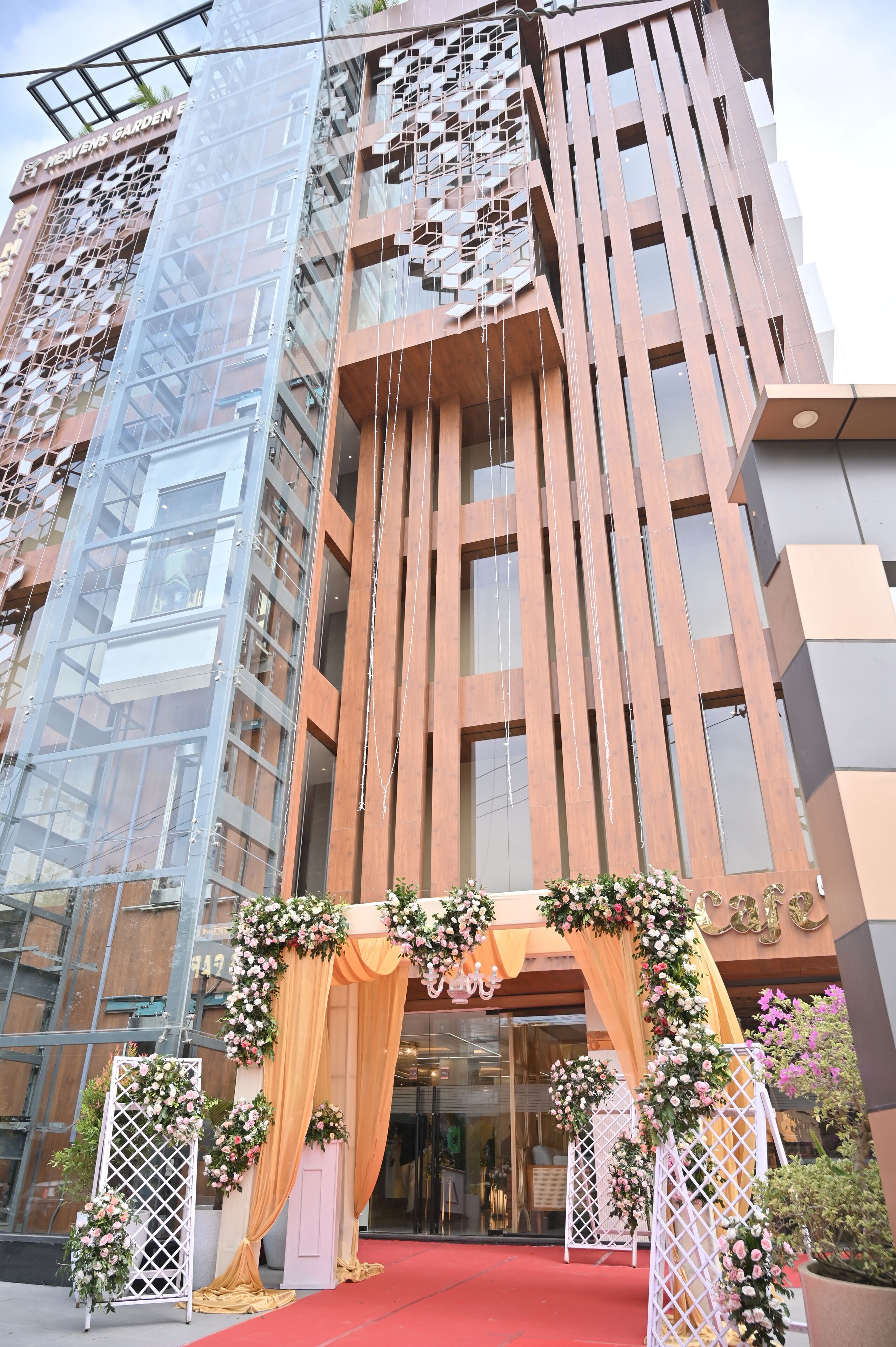 A modern building with a red carpet entrance, glass facade, and decorative floral arrangements.