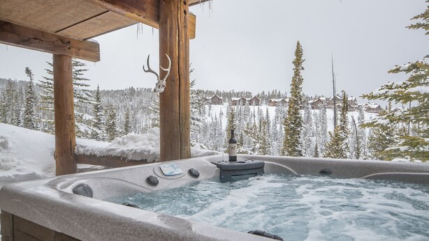 Ein Whirlpool mit Holzkonstruktion und verschneiter Landschaft im Hintergrund.