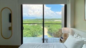 A hotel room with a large bed, a chair, a table, and a view of a green landscape through a large window. - w*| Prestigious 2BR w/ Amazing View in Morros Eos (Cartagena de Indias)