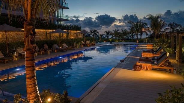 A swimming pool with lounge chairs and umbrellas, surrounded by palm trees and a modern building. - w*| Prestigious 2BR w/ Amazing View in Morros Eos (Cartagena de Indias)