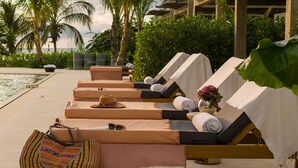 A row of sun loungers with towels and a hat, a bag, and a flower vase on a poolside deck with palm trees and a view of the sea. - w*| Prestigious 2BR w/ Amazing View in Morros Eos (Cartagena de Indias)