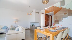 A modern living room with a white sofa, a dining table set with plates and glasses, and a staircase leading to an upper level. - Casa Madeira - Stunning Villa in Carvoeiro (Carvoeiro)