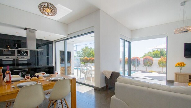 A modern living room with a sofa and dining area, large windows, and a view of the outdoors. - Casa Madeira - Stunning Villa in Carvoeiro (Carvoeiro)