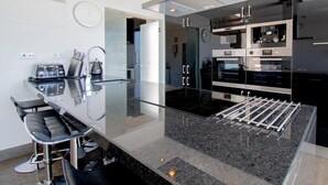 A modern kitchen with a glass dining table, stainless steel appliances, and a built-in oven. - Casa Madeira - Stunning Villa in Carvoeiro (Carvoeiro)