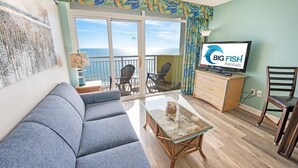 A living room with a sofa, a glass coffee table, a TV, and a balcony with chairs.