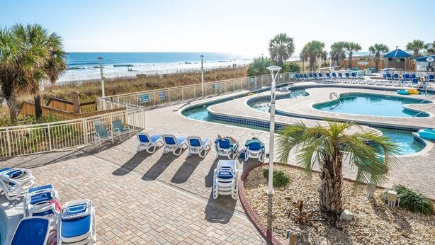 A pool area with lounge chairs and a view of the beach.