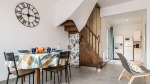 A dining area with a table set for four, a wooden staircase, and a kitchen visible in the background. - Renovated house with wifi, in the heart of St Mars la Jaille (Vallons-de-L'Erdre)