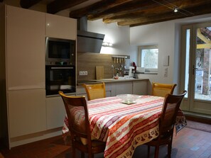 A kitchen with wooden cabinets, a built-in oven, a microwave, and a dining area with a table and chairs.