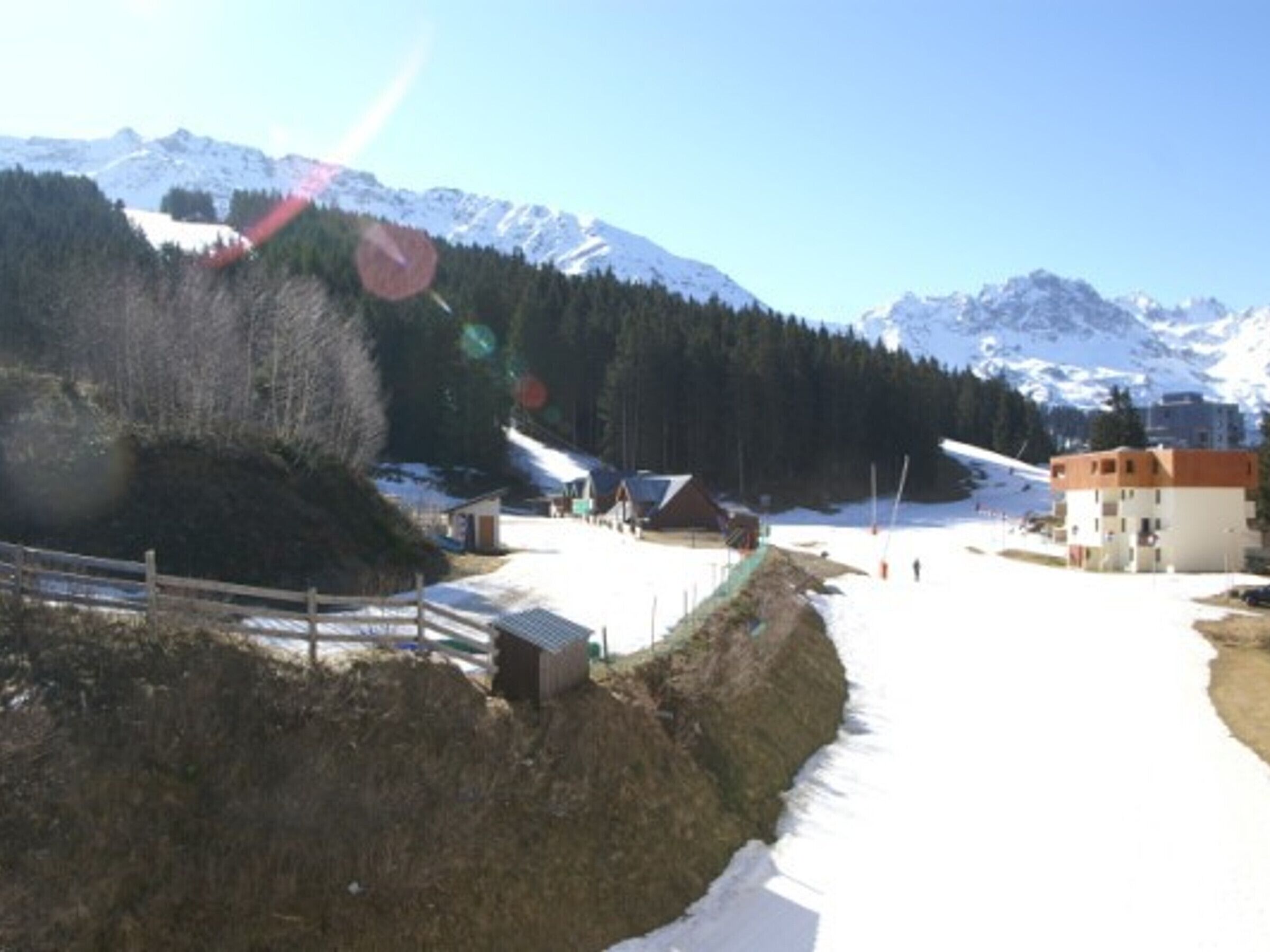 A snow-covered ski slope with buildings and a wooden fence.