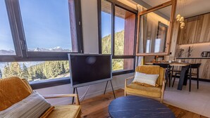 Een gezellige woonkamer met een grote televisie, comfortabele zitplaatsen en uitzicht op bergen.