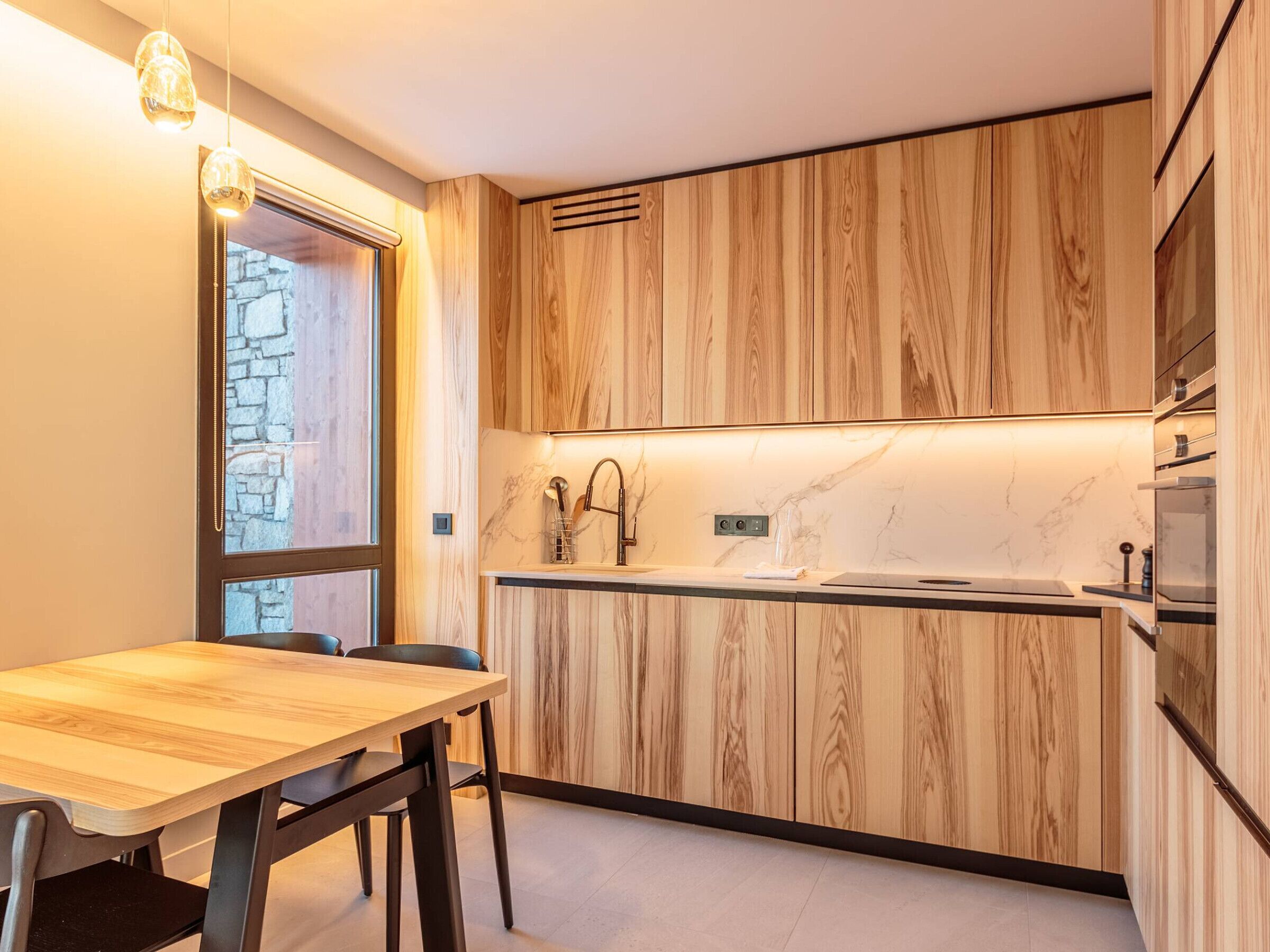 A modern kitchen with wooden cabinetry, a marble countertop, and a built-in oven.