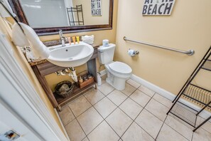 Bathroom with a sink, toilet, and mirror, featuring a towel and handrail for support.