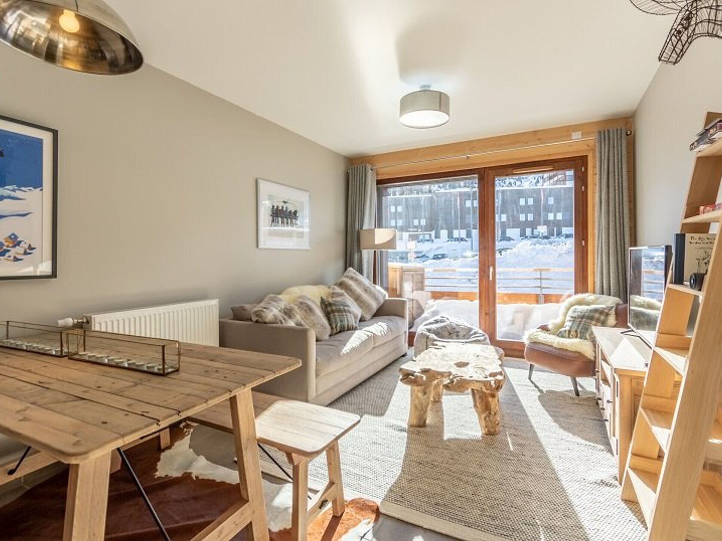 A cozy living room with a wooden table, a sofa, and a view of a snowy landscape through large windows.