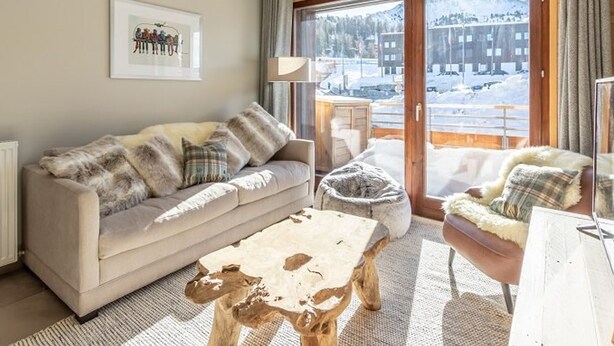 A cozy living room with a sofa, a coffee table, and a chair, featuring a large window with a snowy view.