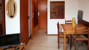 Una habitación con una mesa de comedor de madera, sillas, un televisor y un pasillo que conduce a otra habitación.
