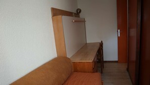 Una habitación con una cama de madera, una mesita de madera y una silla.