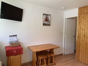A small room with a wooden table and stools, a television mounted on the wall, a framed picture, and a door with a wooden panel. - Cozy studio near slopes at Plagne Centre, 4 pers. (La Plagne-Tarentaise)