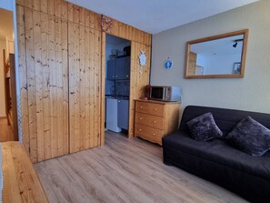 A compact living space with a wooden wardrobe, a kitchenette, a black sofa, and a mirror on the wall. - Cozy studio near slopes at Plagne Centre, 4 pers. (La Plagne-Tarentaise)